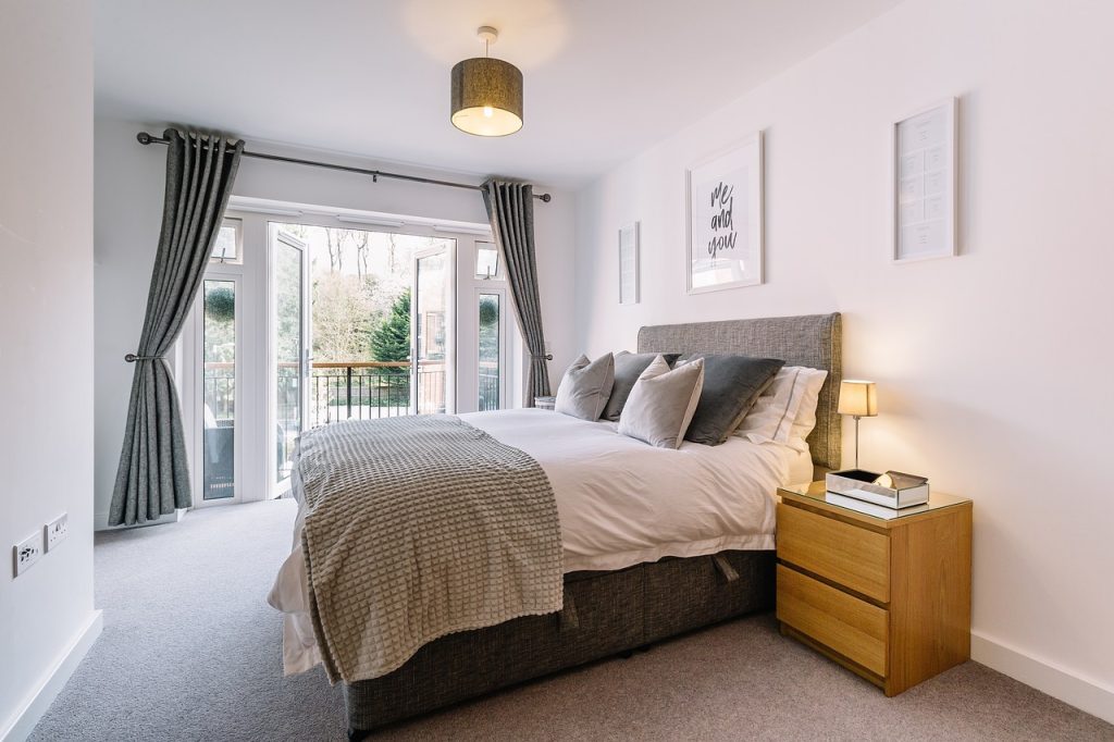 A serene bedroom scene showcasing a bed, a nightstand, and a sliding glass door that opens to a balcony