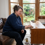 A woman relaxes on a couch in a stylish living room, with soft furnishings and a welcoming atmosphere